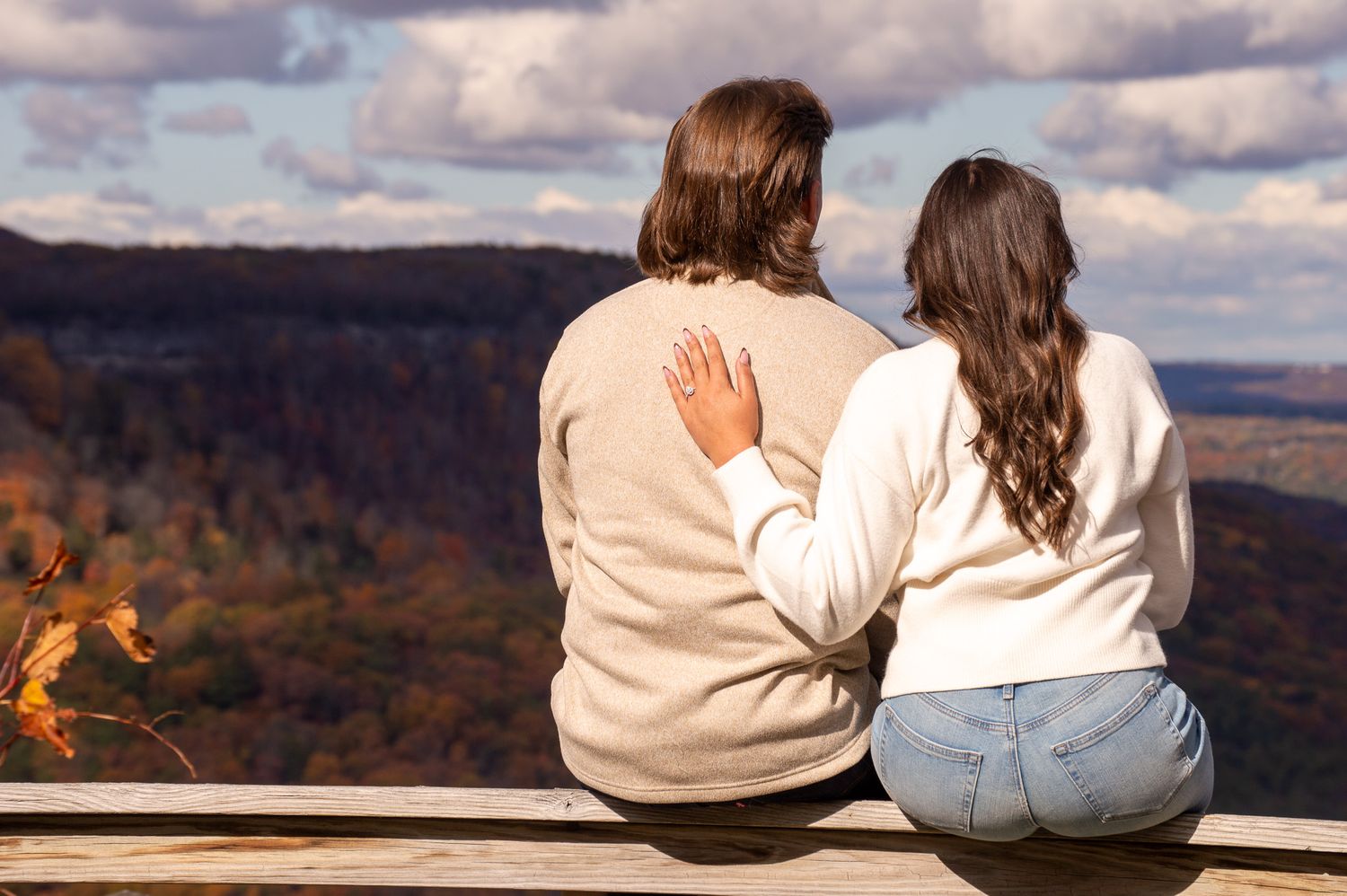 People sitting close together on a bench overlooking a scenic mountain landscape with dramatic clouds.