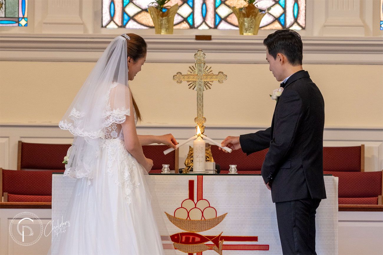 A couple stands at the altar during their wedding ceremony in an elegant church with stained glass windows.