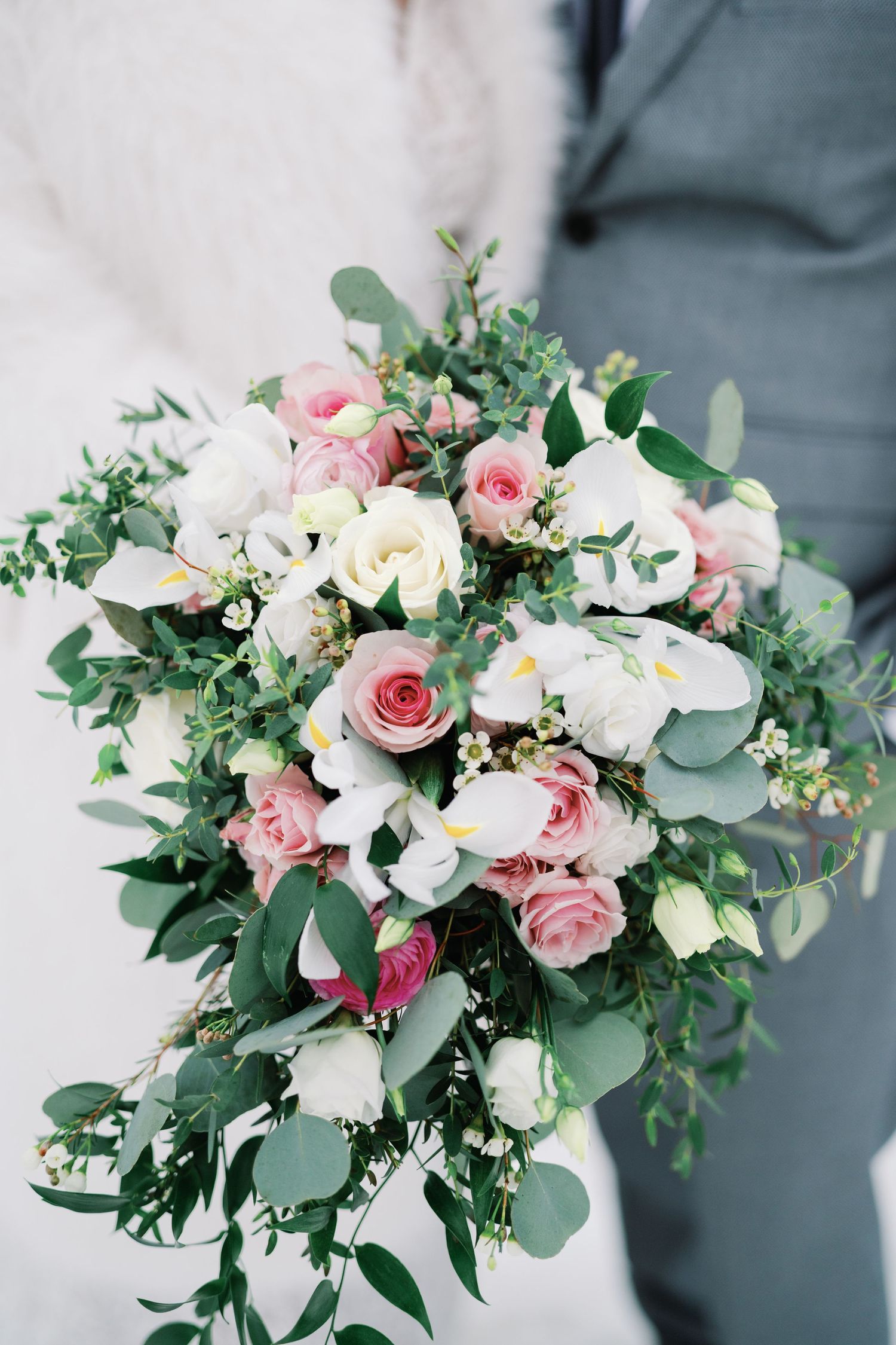 Wedding bouquet featuring soft pink roses, white flowers and eucalyptus greenery against a gray background.