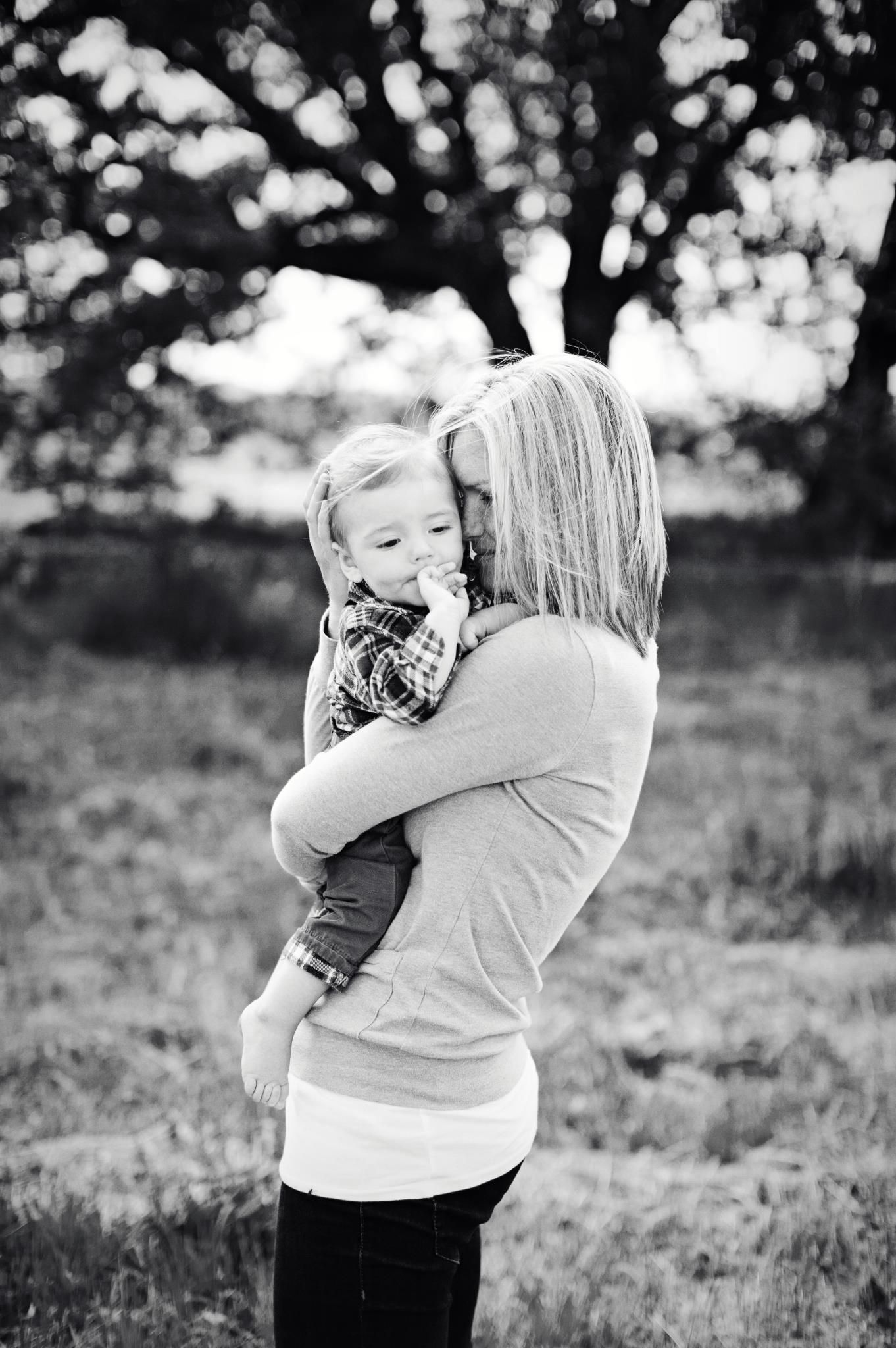 Mother hugging toddler in plaid scarf in black and white outdoor field photo.
