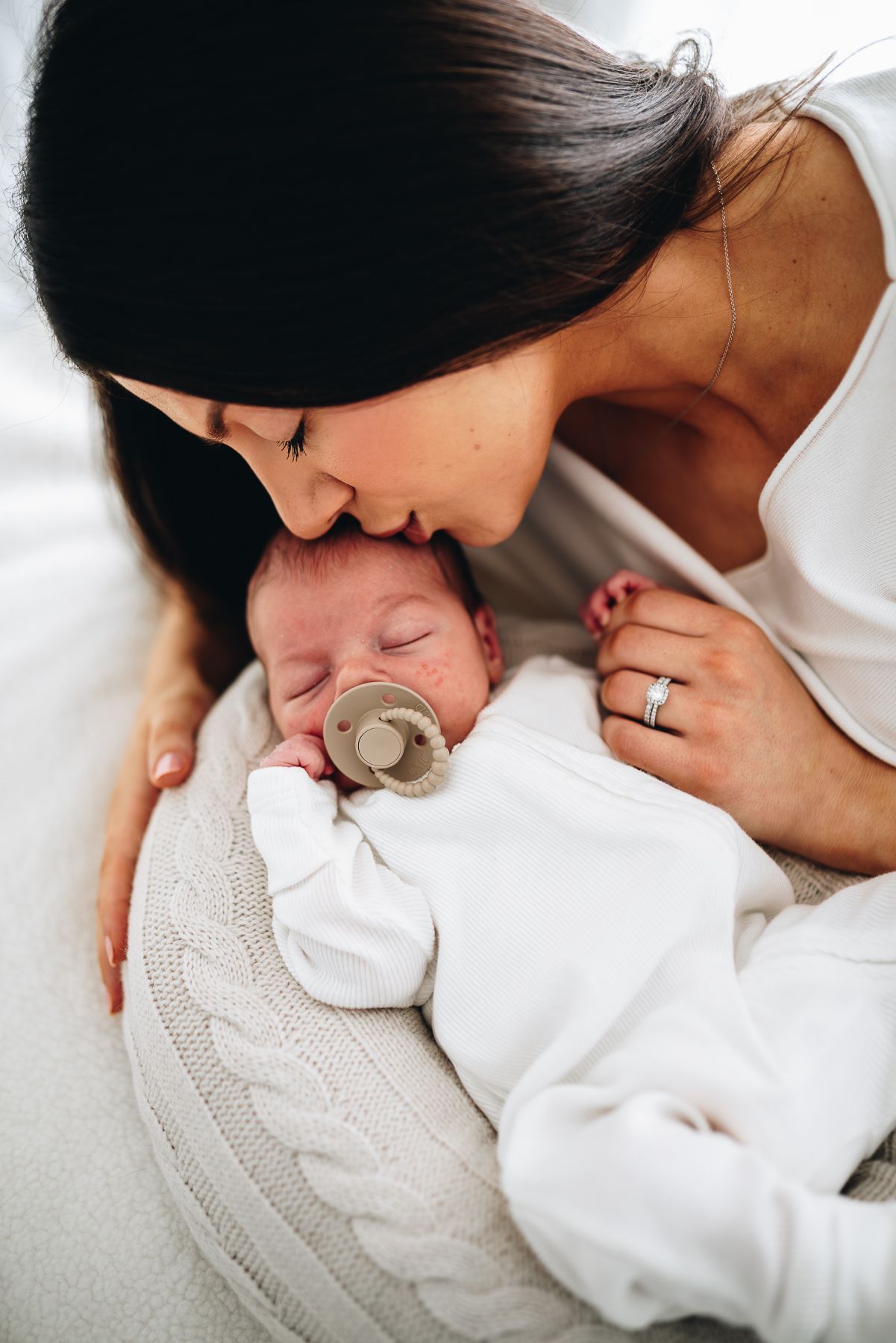 A tender moment between mother and baby in white clothing showing gentle affection and bonding during a Melbourne newborn photo session.