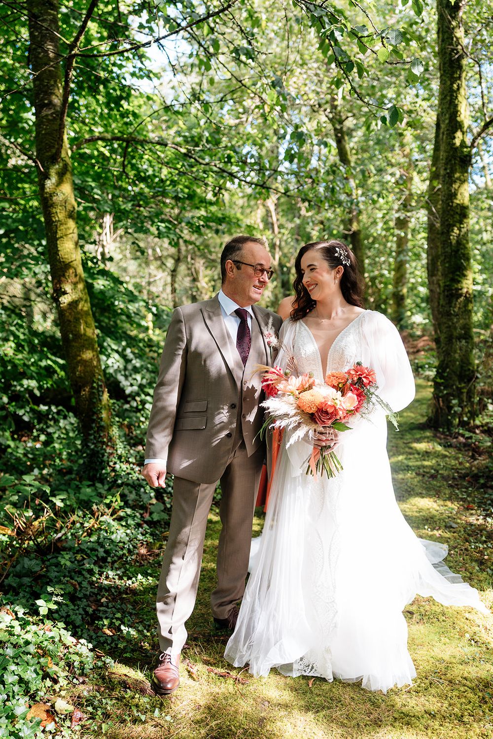 A couple shares romantic moments in a sunlit wooded area during their wedding celebration.