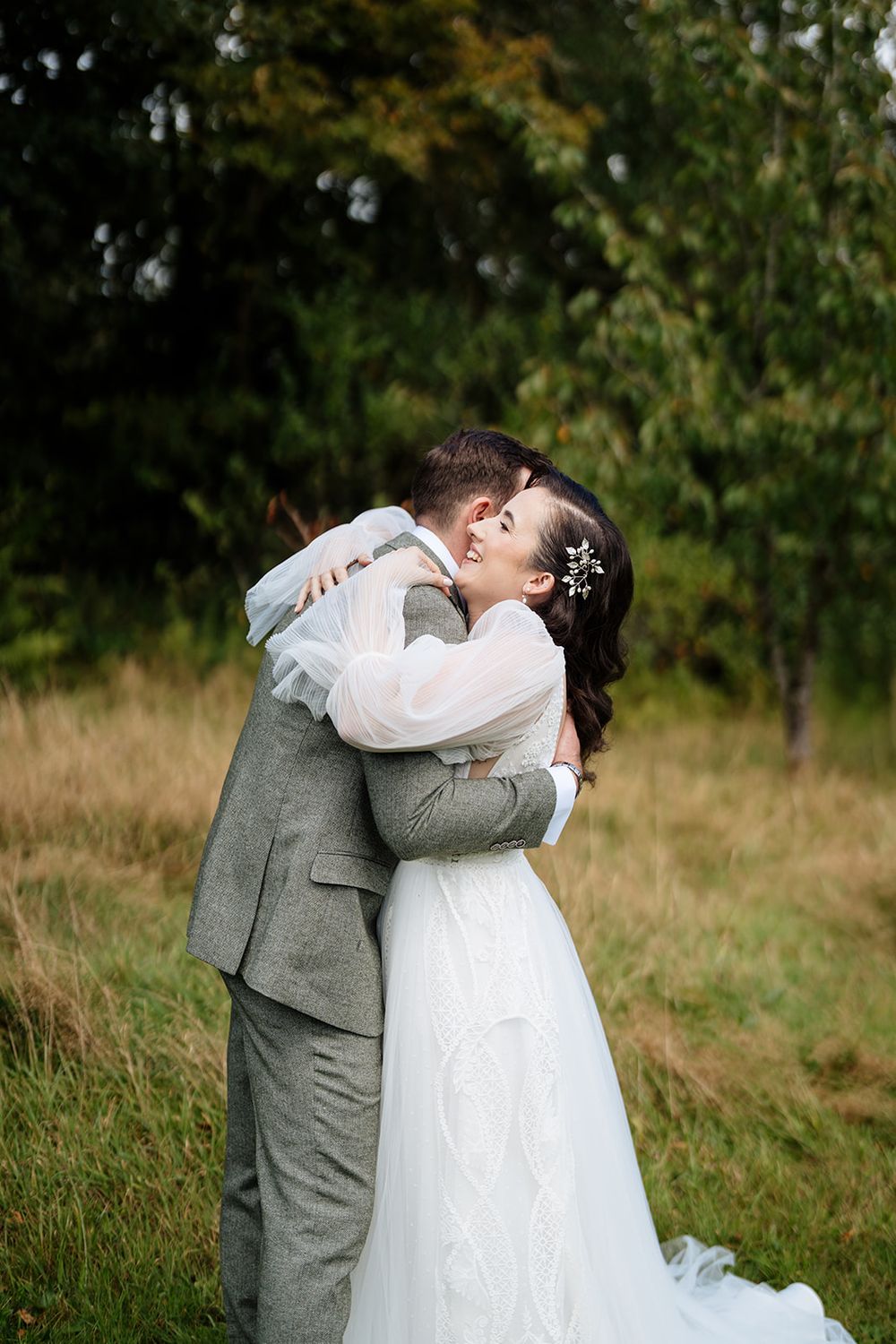 A couple embraces in a romantic moment outdoors with green foliage and natural scenery in the background.