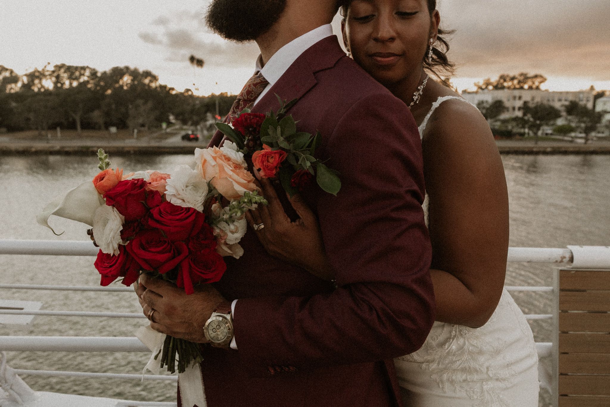 Bride and Groom embracing during sunset portraits on a yacht with red and white floral bouquet