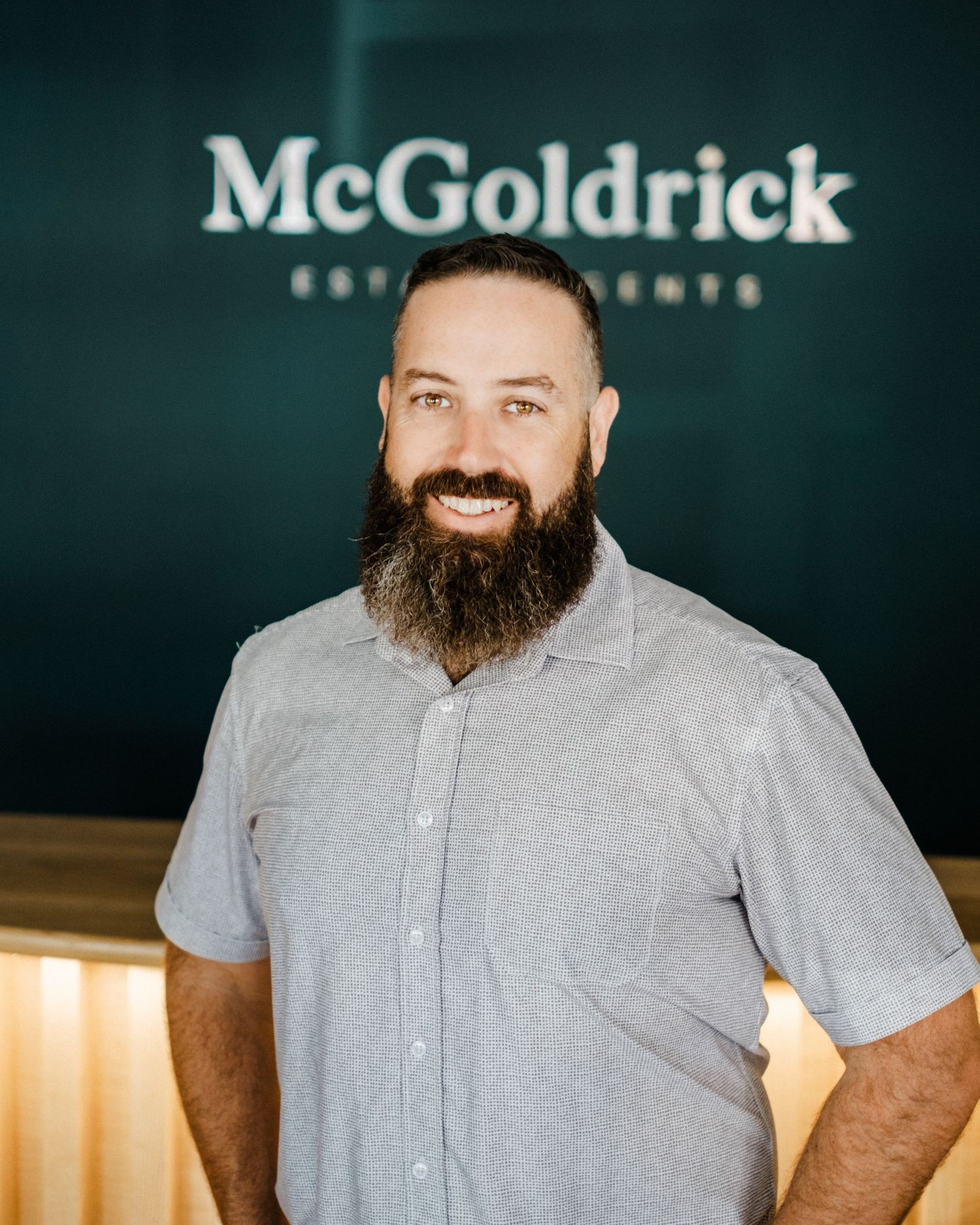 Professional business portrait showing a smiling person in a black shirt against a green McGoldrick branded wall.
