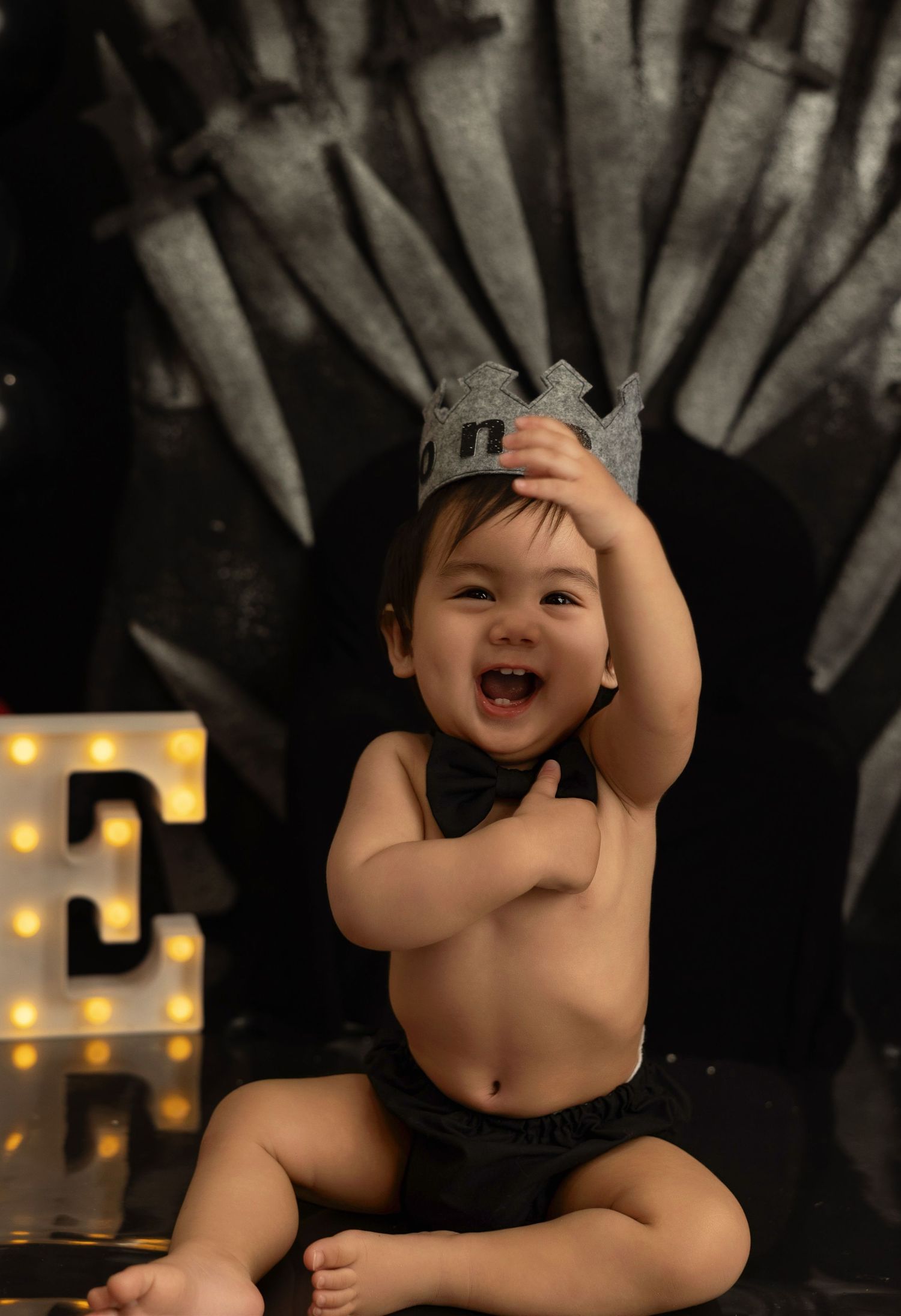 A laughing baby sits against a dark background with illuminated letters visible in the background.