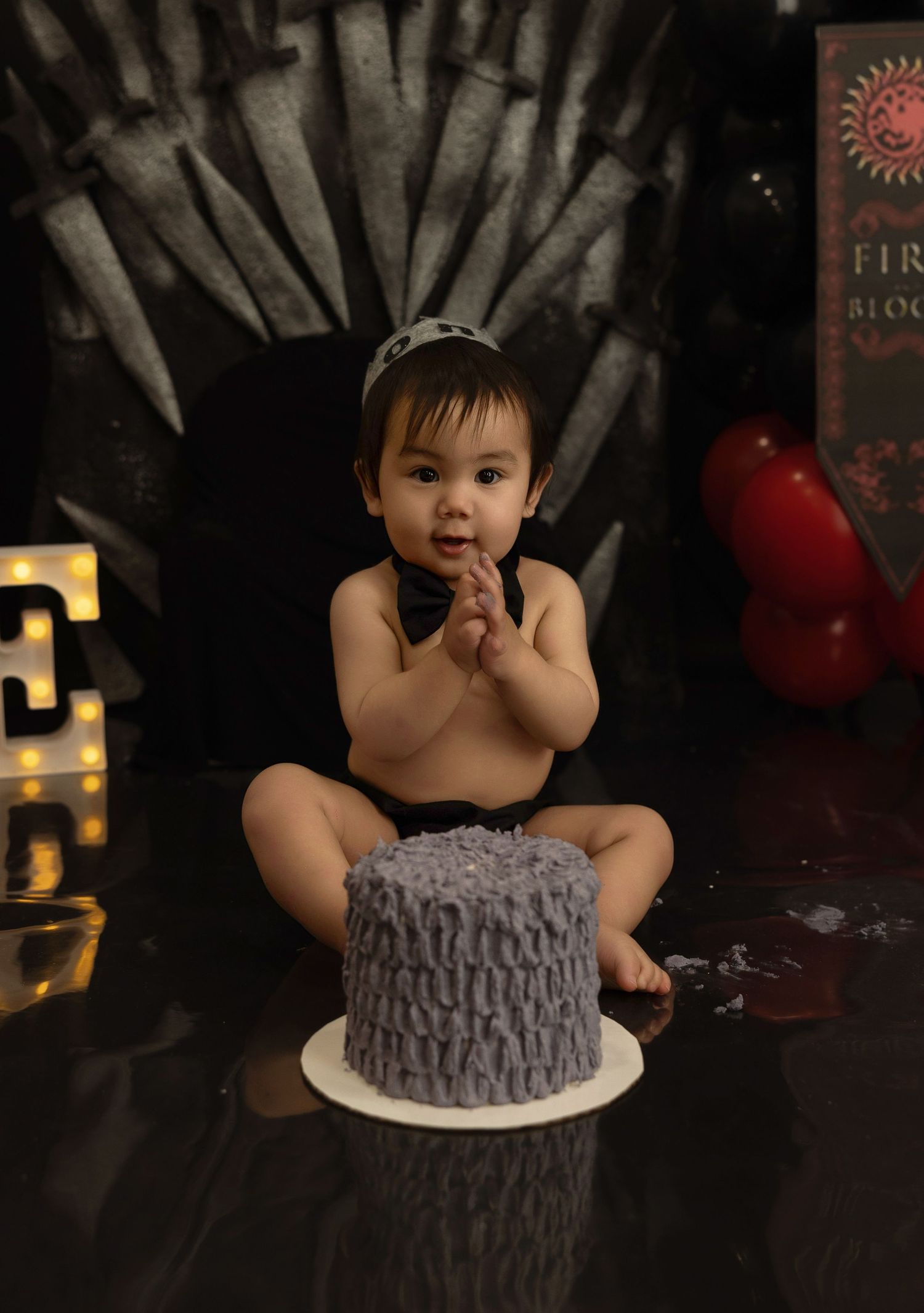 A series of photos showing a baby in a black dress next to a gray textured birthday cake against a dark background.