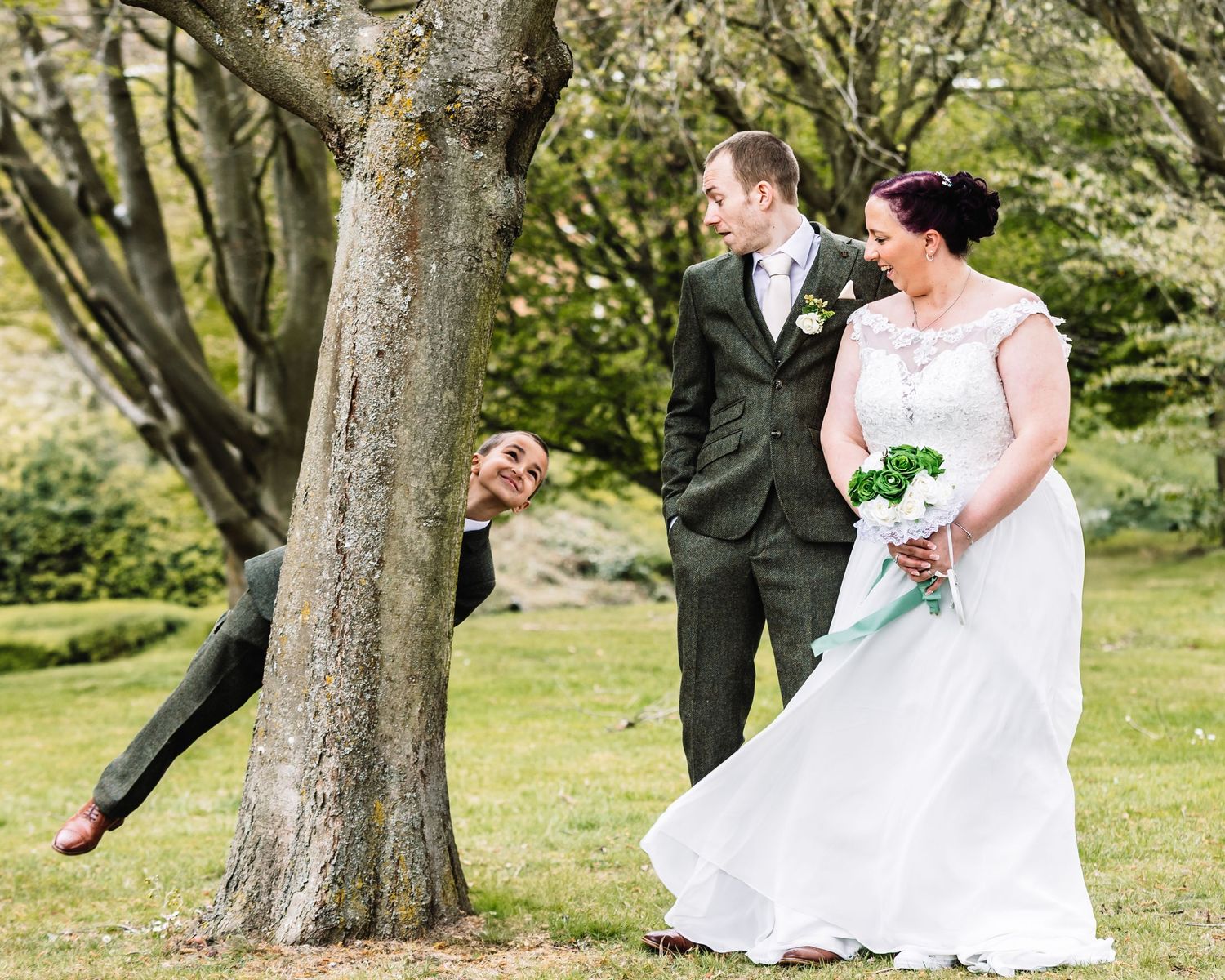 A couple in formal wedding attire shares a romantic moment while dancing outdoors among trees in a garden setting.