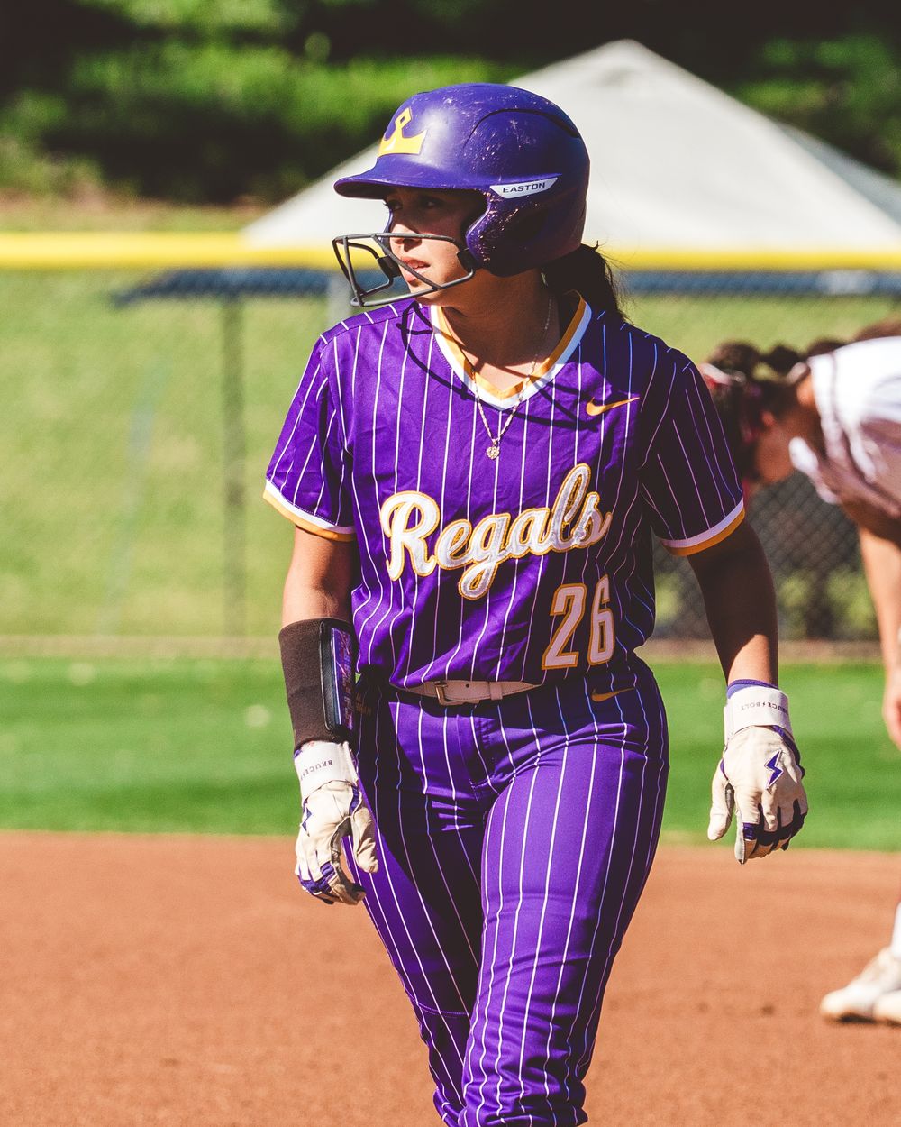 Baseball player in purple pinstriped uniform running on dirt field during game.