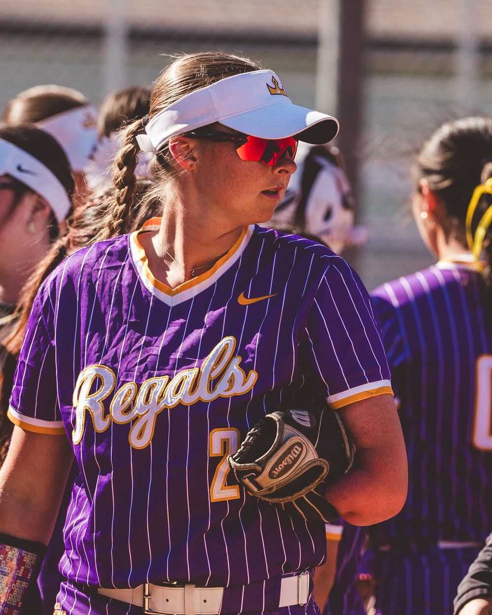 Baseball team members in purple striped jerseys gather in the dugout during a game.