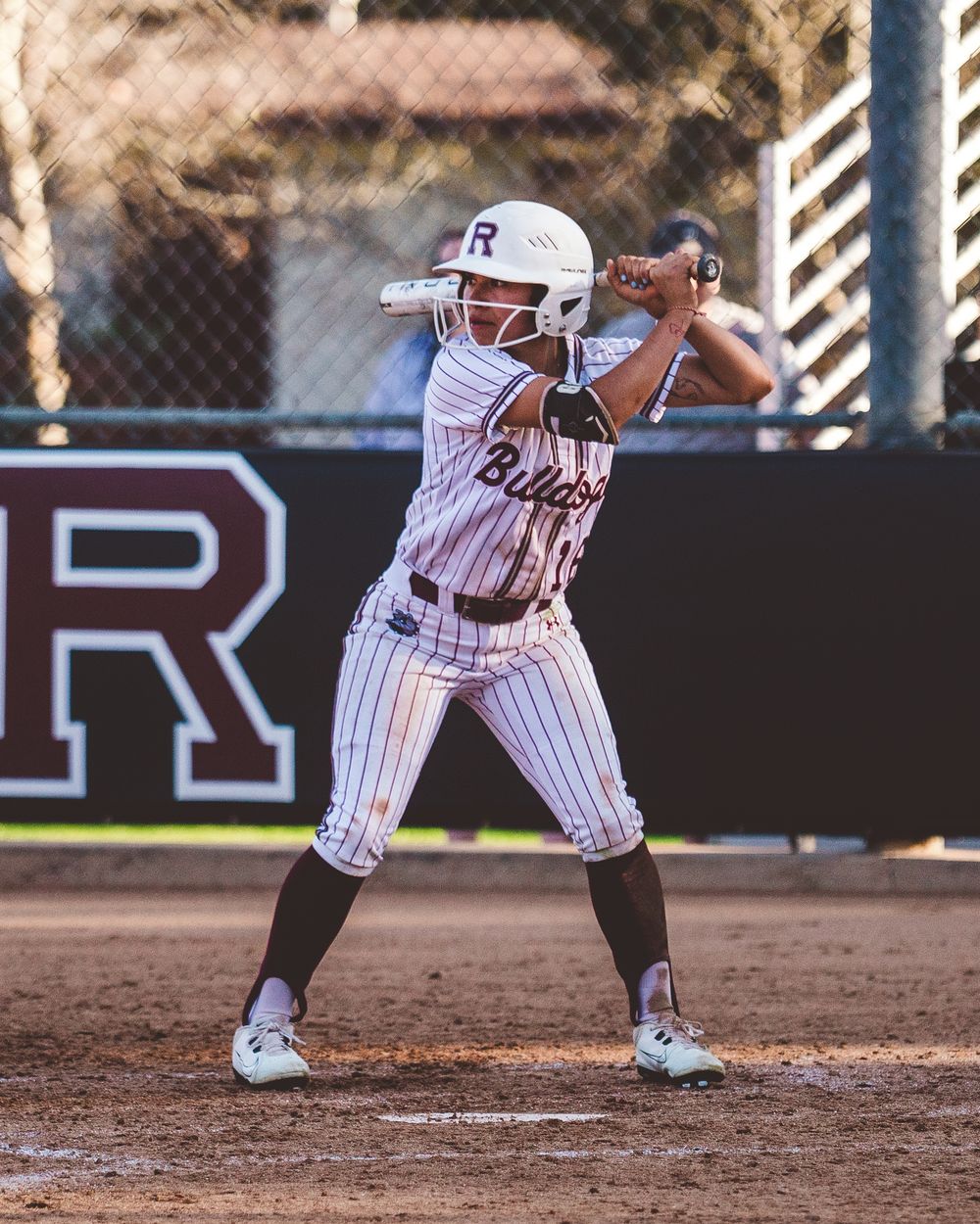 Softball player crouches in batting stance on dirt field during game action.