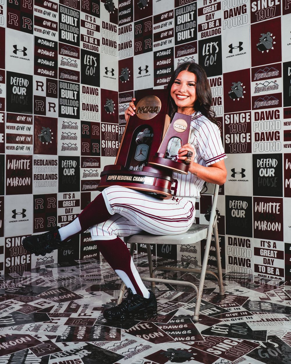 Baseball themed photo shoot setup with Under Armour logos and motivational text on backdrop wall.