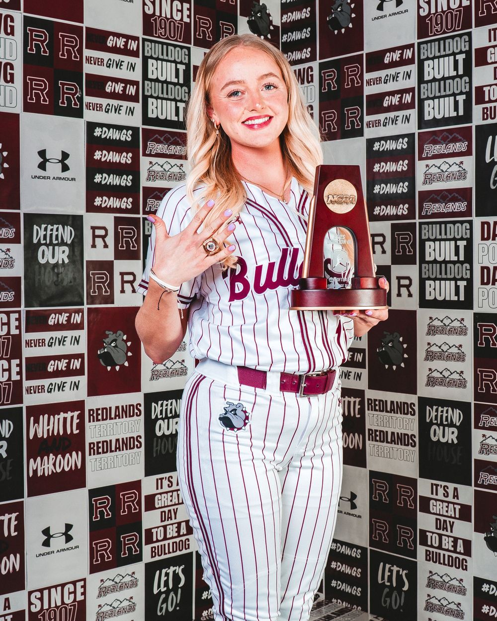 Baseball player in pinstriped uniform poses against a branded sponsor wall with Under Armour and team logos.