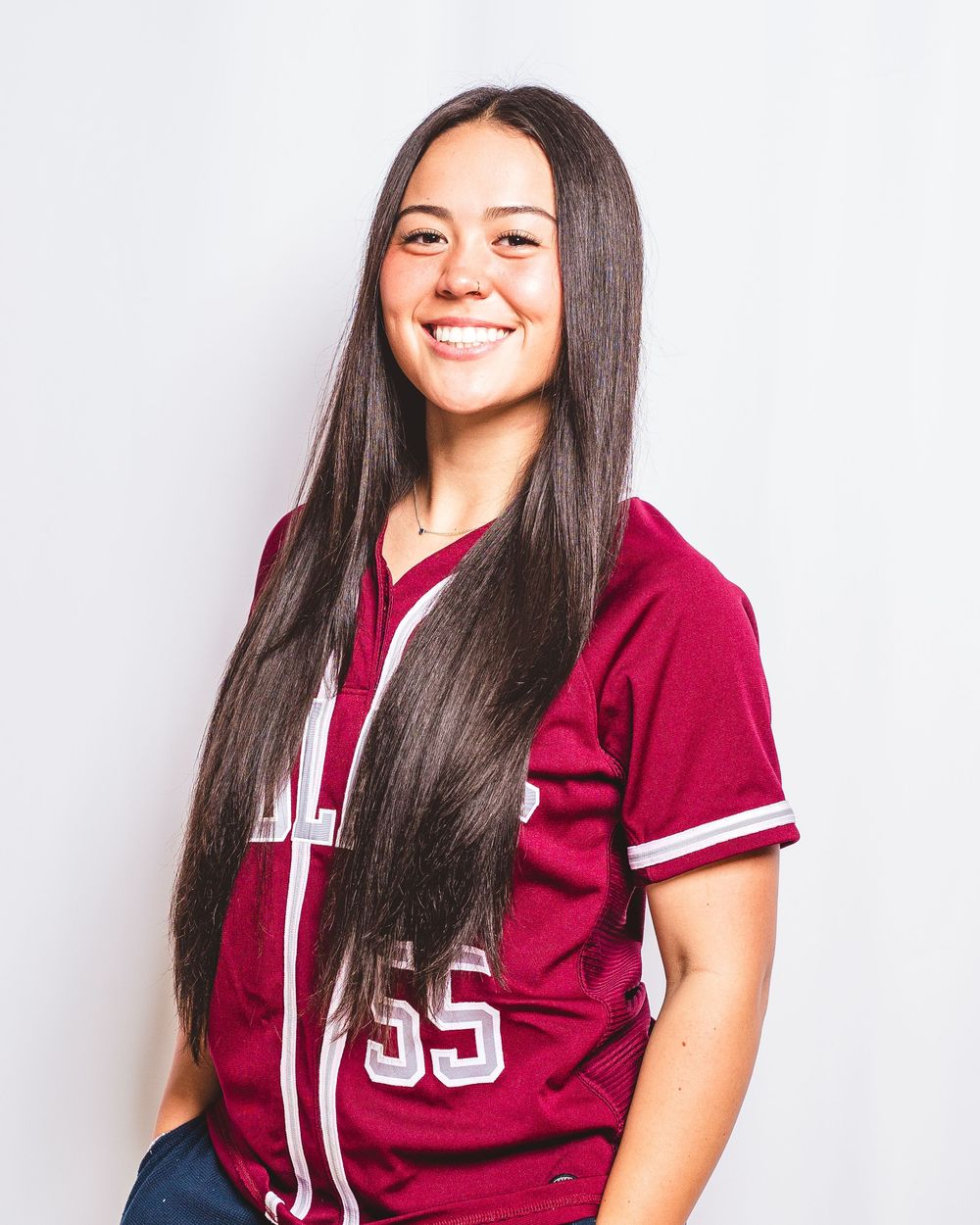 Athlete in burgundy baseball jersey number 55 with long dark hair poses against light background for portrait photo.