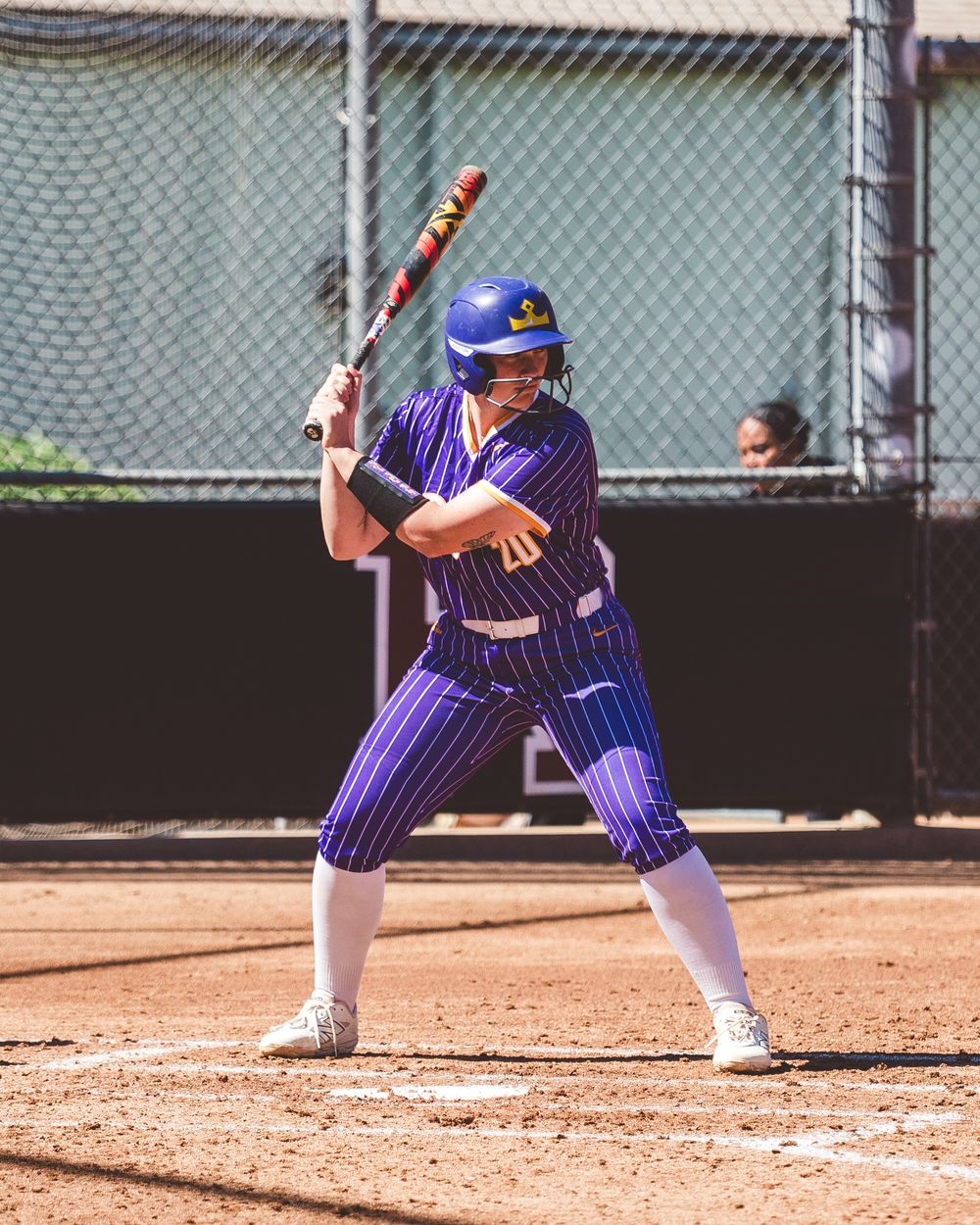 Baseball player in purple pinstripe uniform demonstrates batting stance sequence on dirt field during practice.