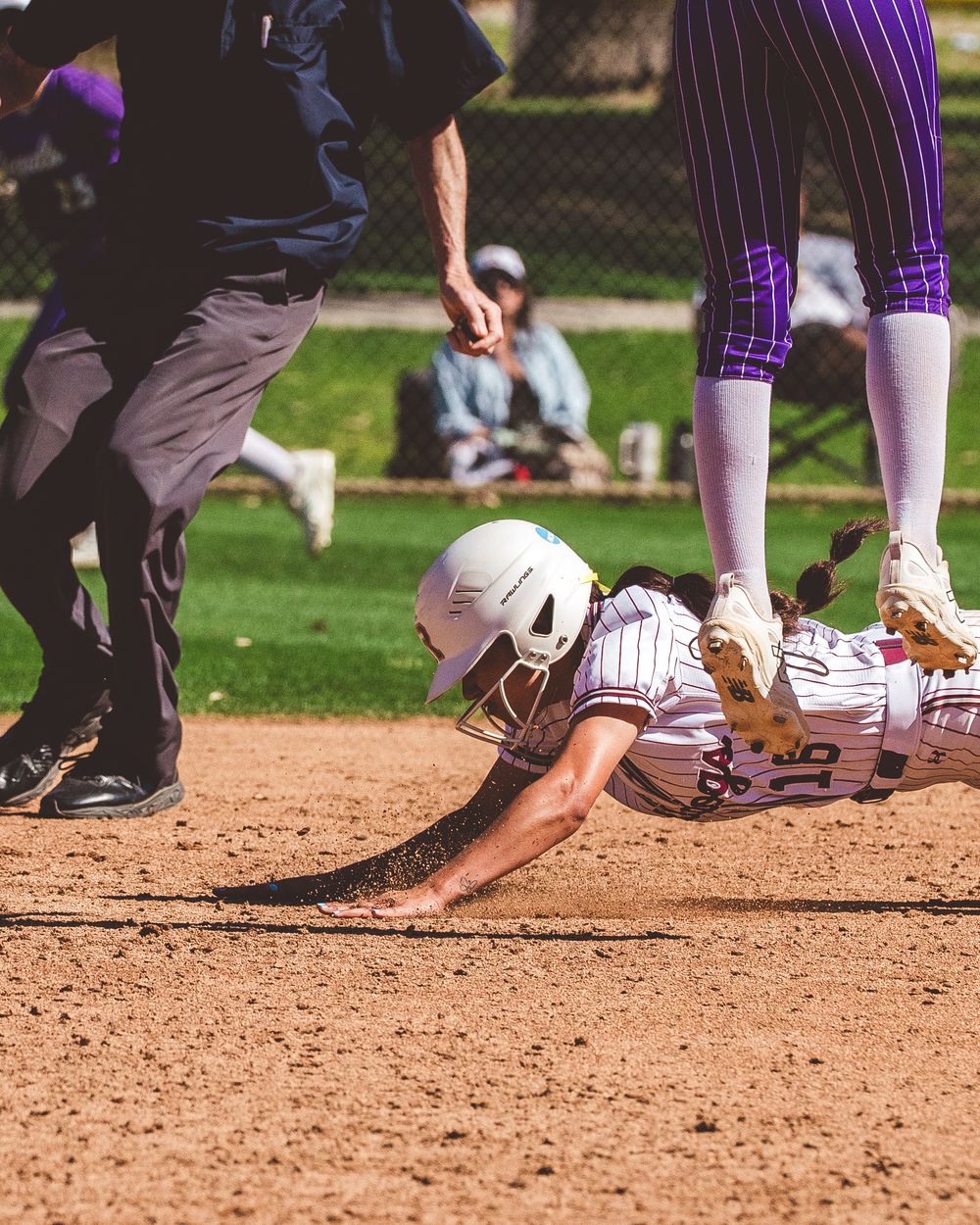 Close-up of baseball players' feet and legs sliding on dirt infield during game action.