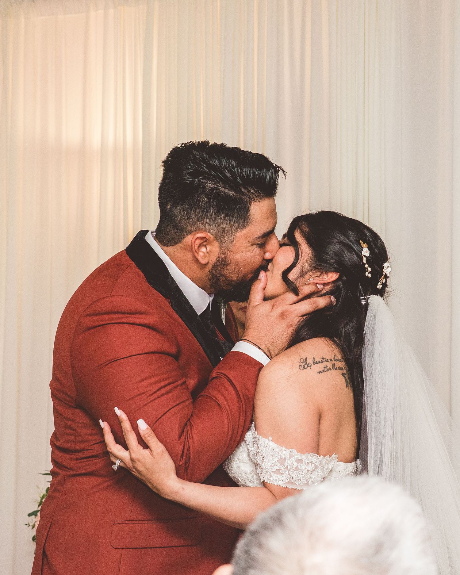 A couple shares three romantic kisses while wearing burgundy and white formal attire.