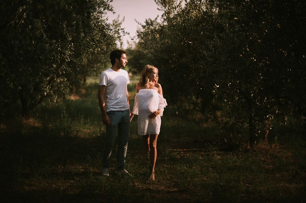 A couple walks hand in hand through an orchard at sunset creating a romantic silhouette against the evening sky.