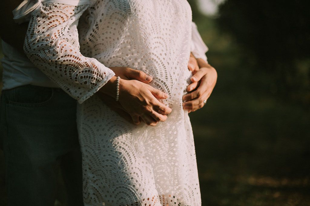 A close-up shot of a delicate white lace maternity dress against a dark background.