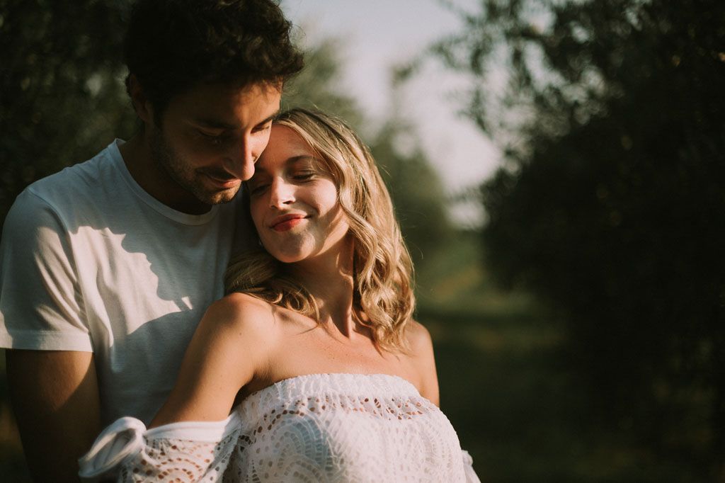Romantic couple embraces in golden sunlight against blurred natural background.
