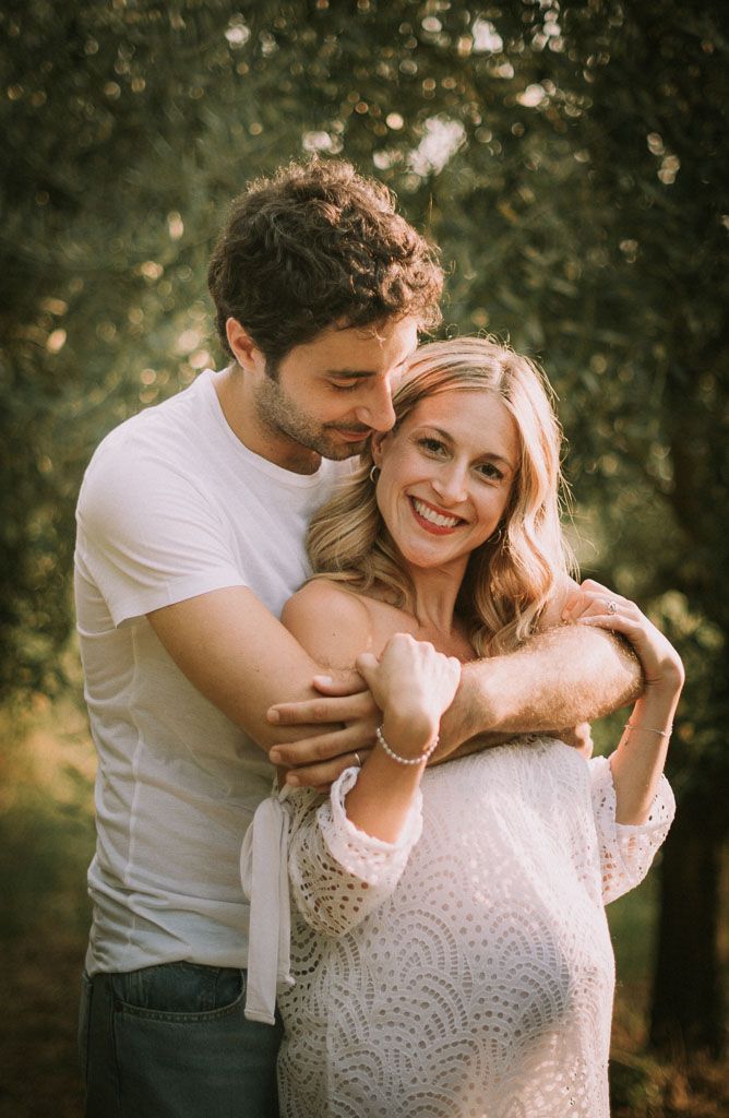 A tender outdoor maternity photoshoot featuring a couple embracing in natural sunlight.