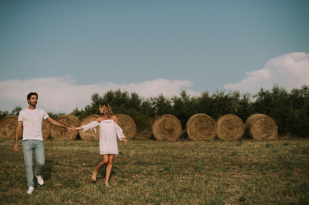 People in white clothing walking through a field with hay bales in the background.