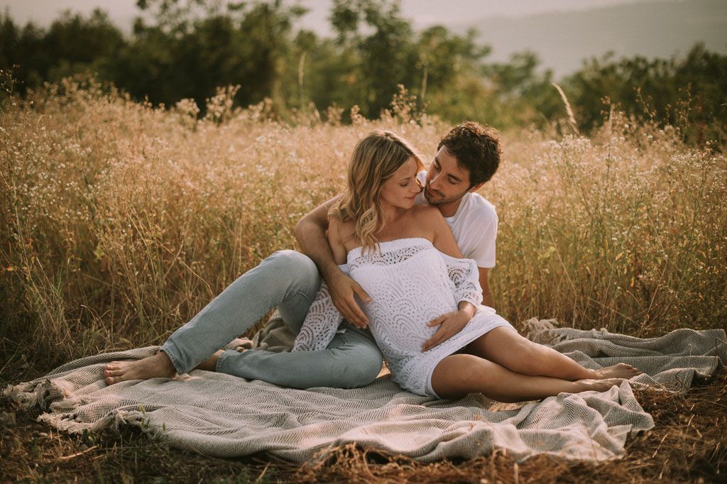 Romantic couple lounging on white blanket in golden field during sunset photoshoot.
