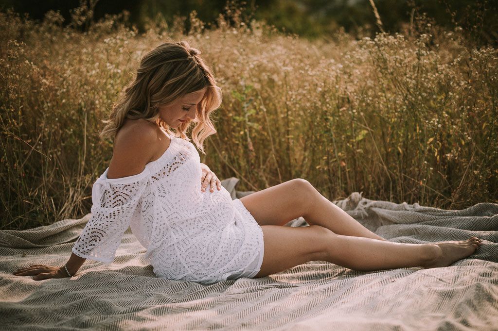 Intimate outdoor portrait session with couple laying on white blanket surrounded by dry grass.
