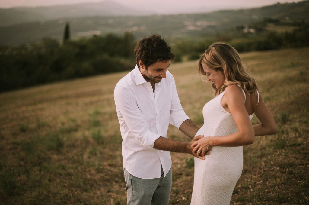 Couple in white outfits dancing together on a grassy hillside at sunset.
