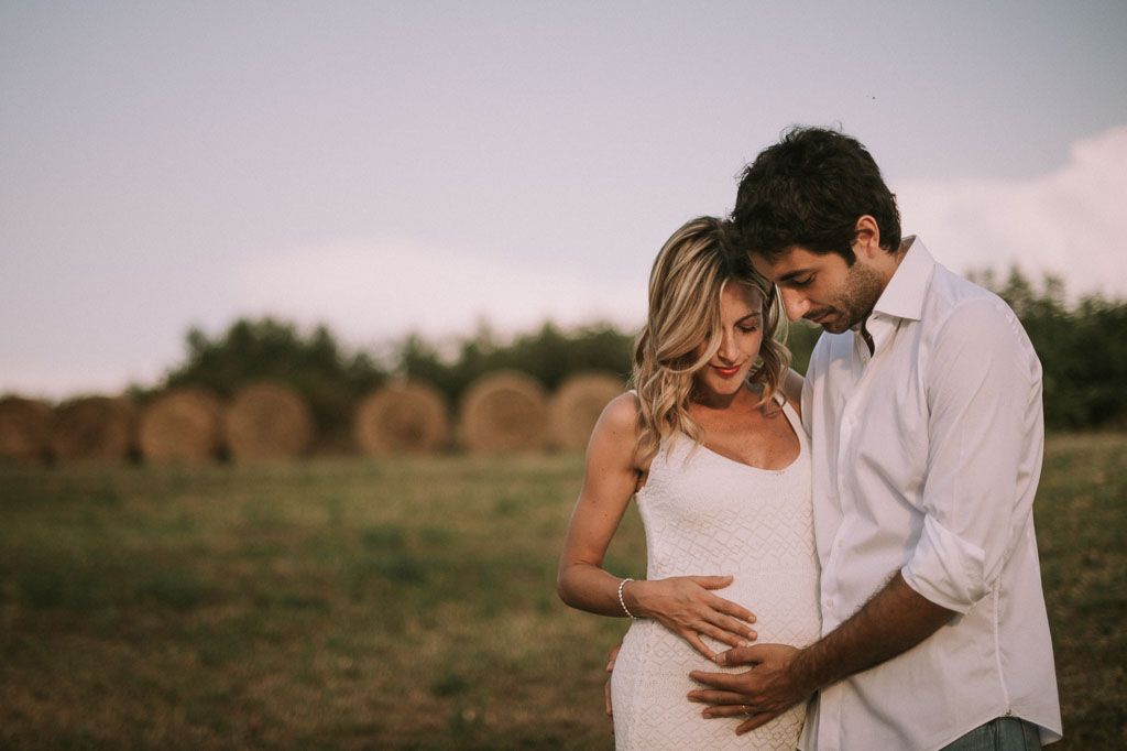 Tender maternity moment captured in outdoor setting with couple in white and denim.
