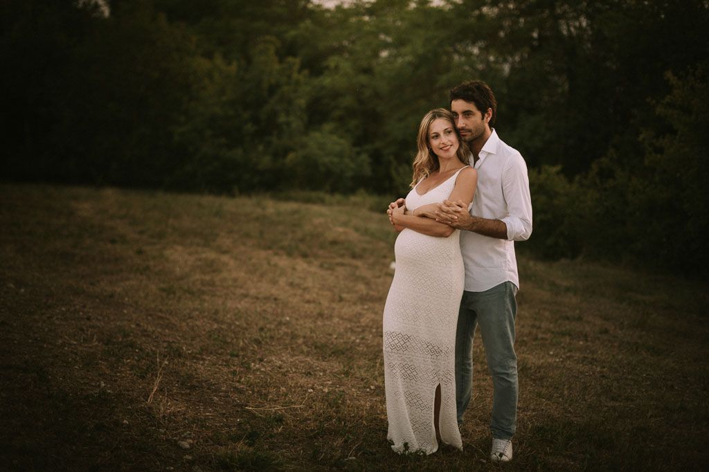 A romantic couple embraces in a golden field during sunset for their engagement photos.