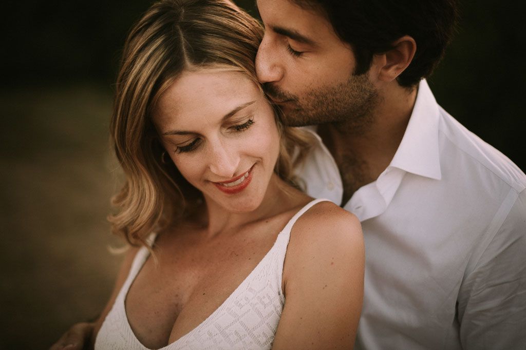A tender moment between a couple sharing intimate poses against a dark moody background.