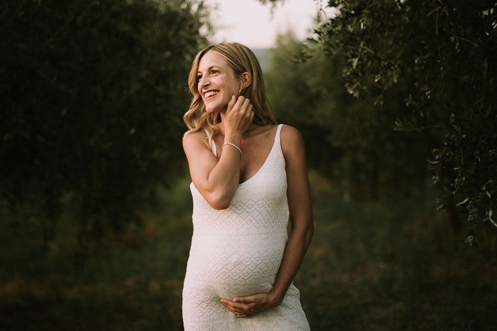 Maternity portrait of woman in white dress against natural backdrop.