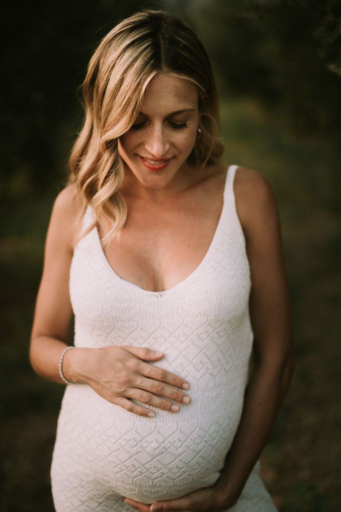 Maternity photo of woman in white lace dress touching her baby bump.