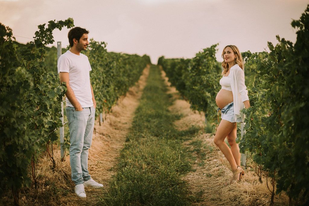 Couple shares tender moment while standing between rows of grapevines in a vineyard at dusk.