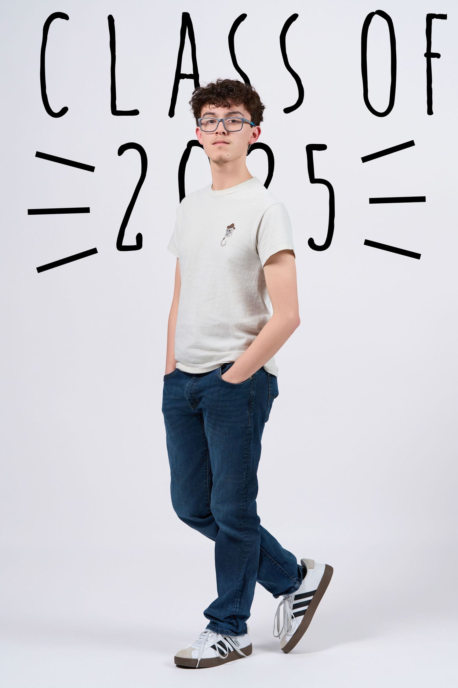 A student in glasses, white t-shirt and jeans poses for Class of 2025 photo against white background.