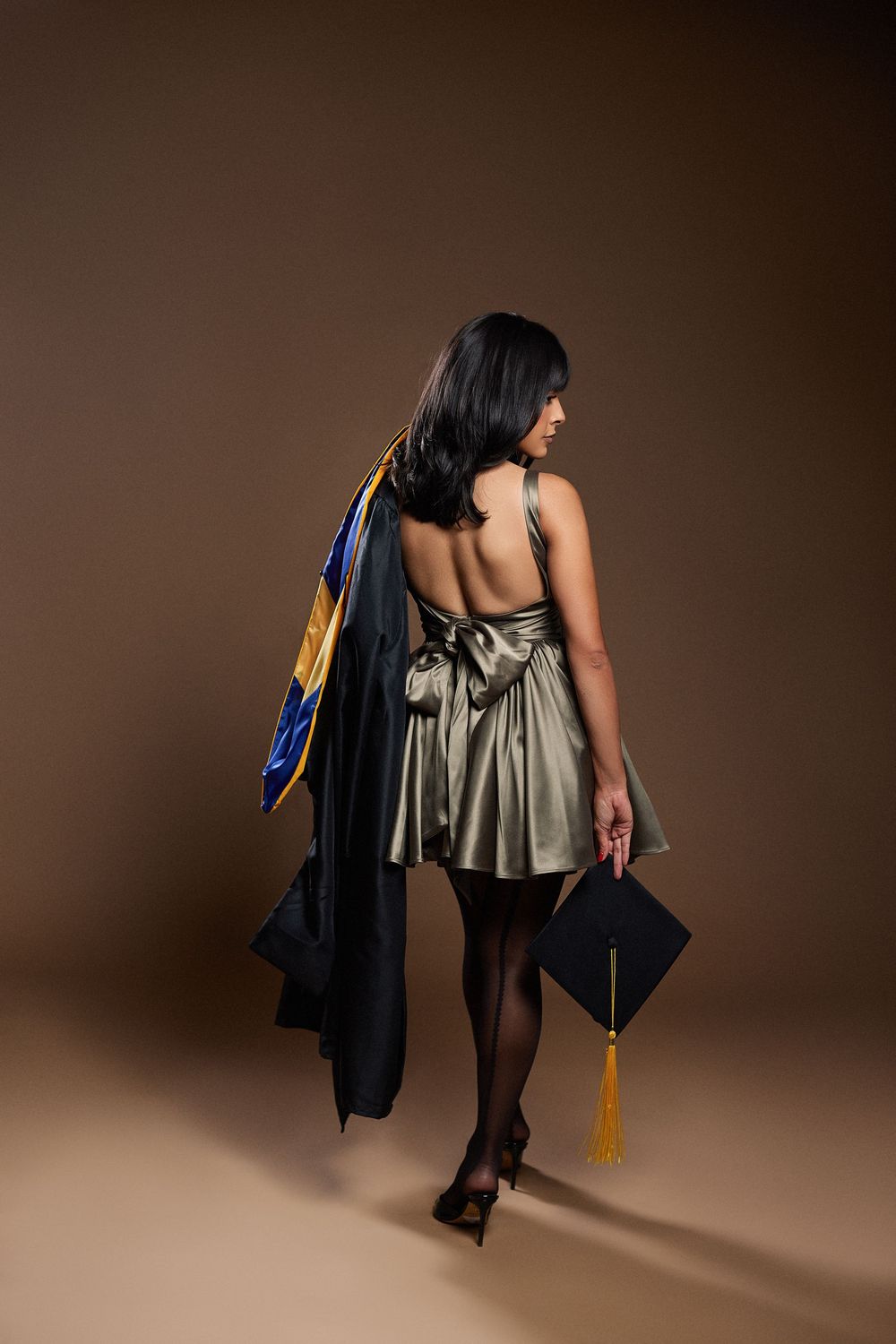 Figure in metallic dress and graduation cap creates dynamic poses in studio.