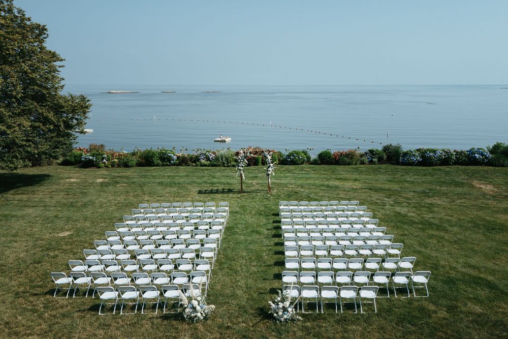 White chairs arranged in rows on a lush green lawn with ocean views for an outdoor wedding ceremony.