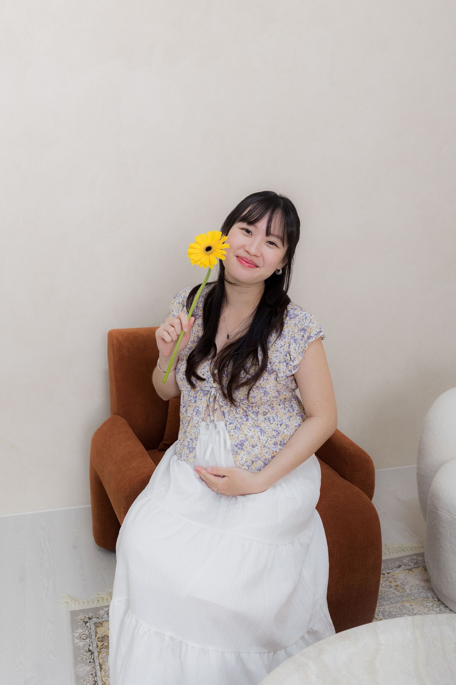 Whimsical portrait session with yellow flower and white dress in brown chair.