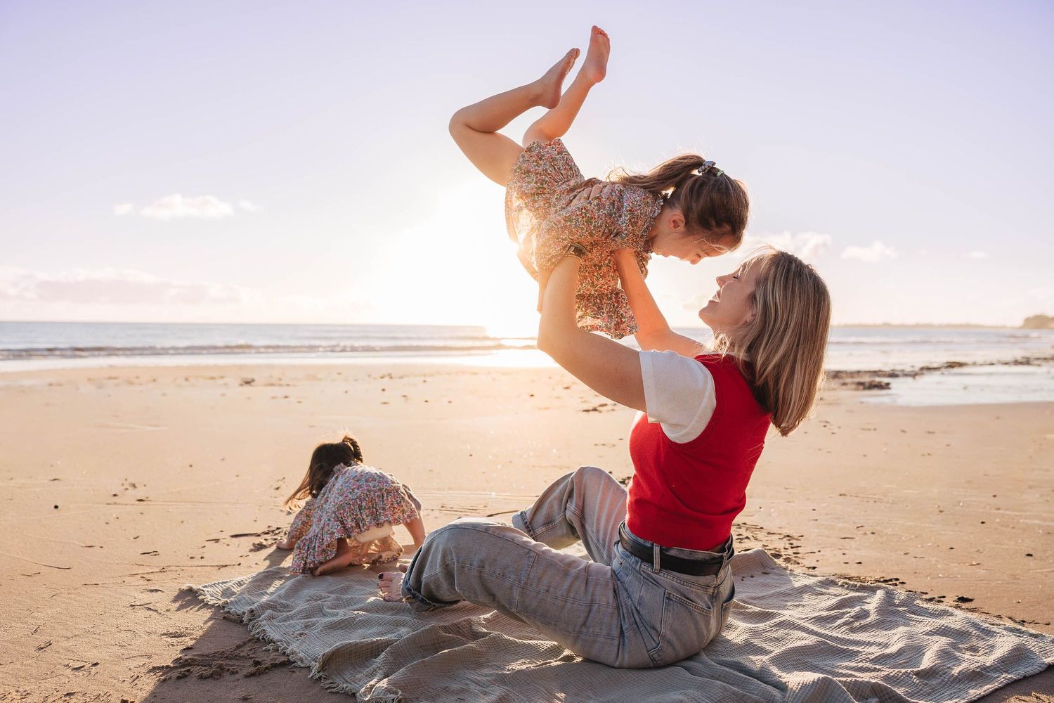 A parent and child play together on a sandy beach at sunset, lifting and bonding in joyful movement.