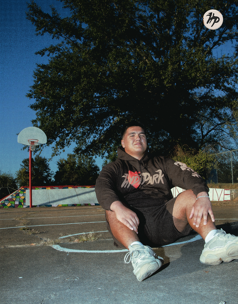 Skateboarder lying down on concrete surface near basketball court at dusk.
