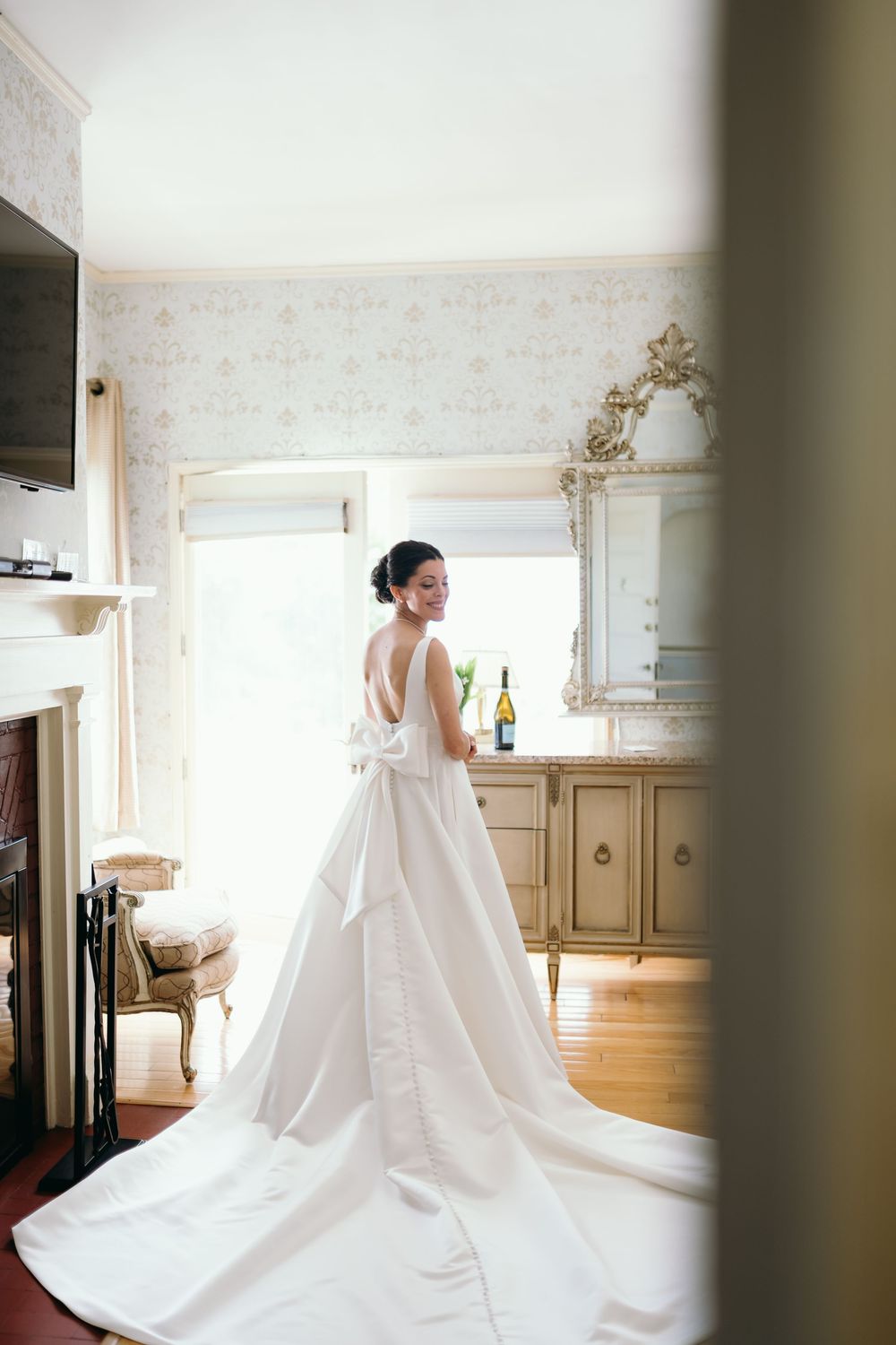 An elegant white wedding gown with a dramatic train is displayed in a beautifully lit bridal preparation room.