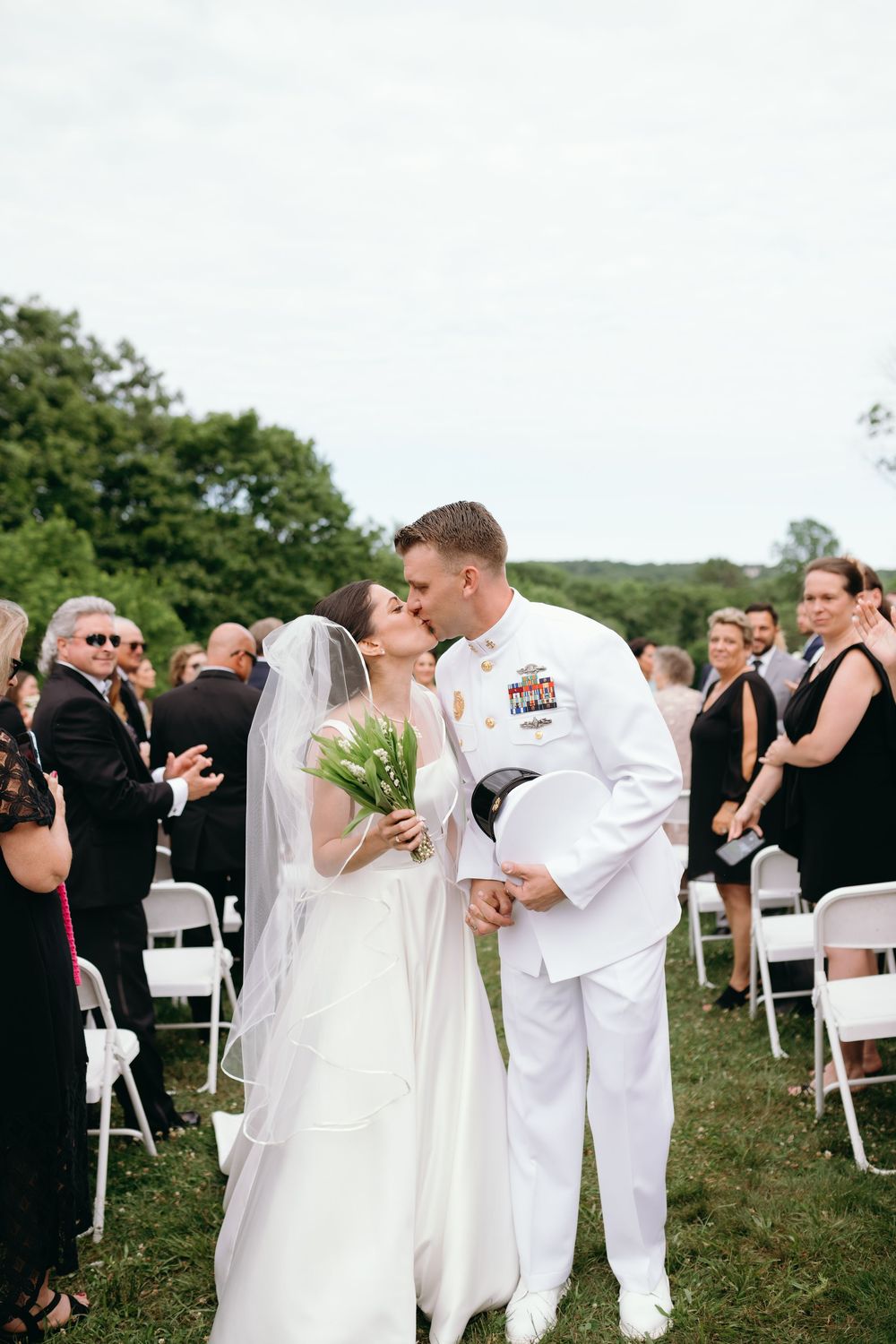 A series of outdoor wedding ceremony photos showing a couple in white exchanging vows and kissing in front of seated guests.