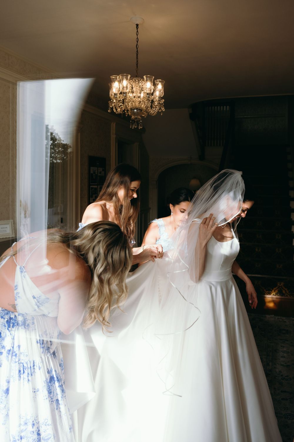 Artistic sequence of a wedding dress being put on in a dimly lit room with a chandelier.
