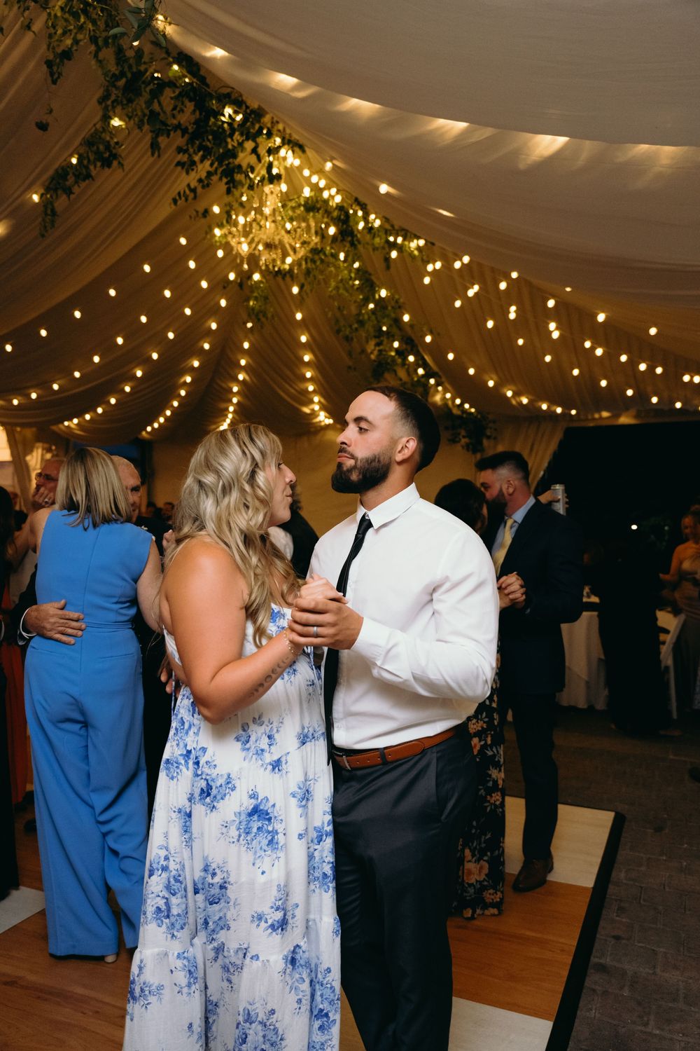 Couples dancing at a wedding reception under string lights and draped fabric.