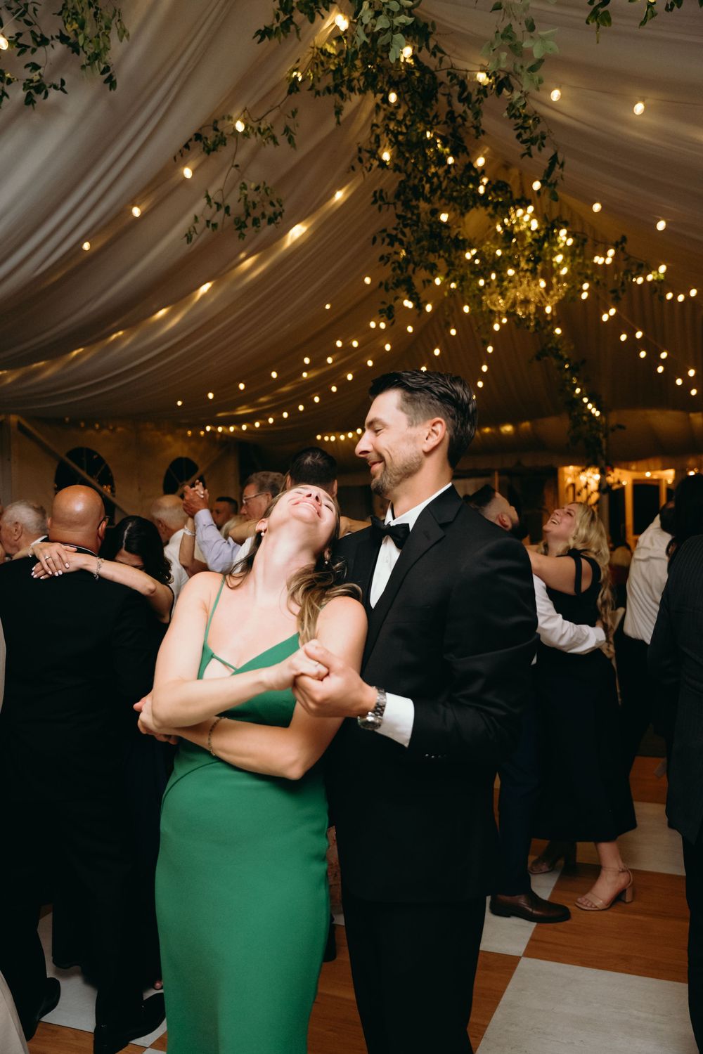 Couples dancing under twinkling lights at an elegant tented wedding reception.