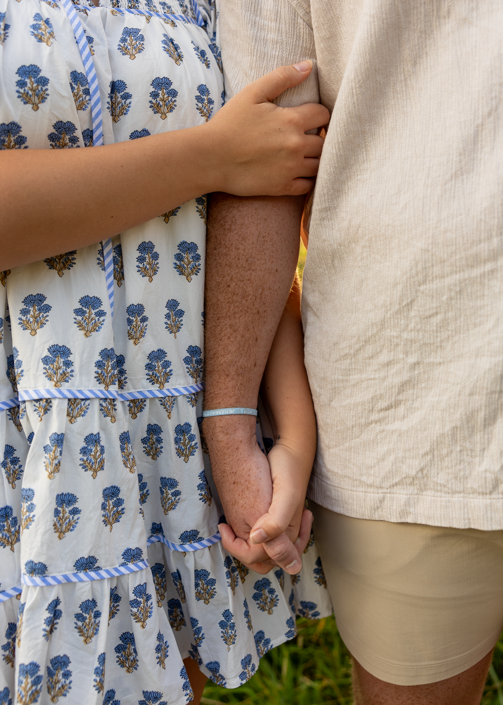 Close-up of a couple holding hands, woman in a blue floral dress and man in a beige linen shirt.
