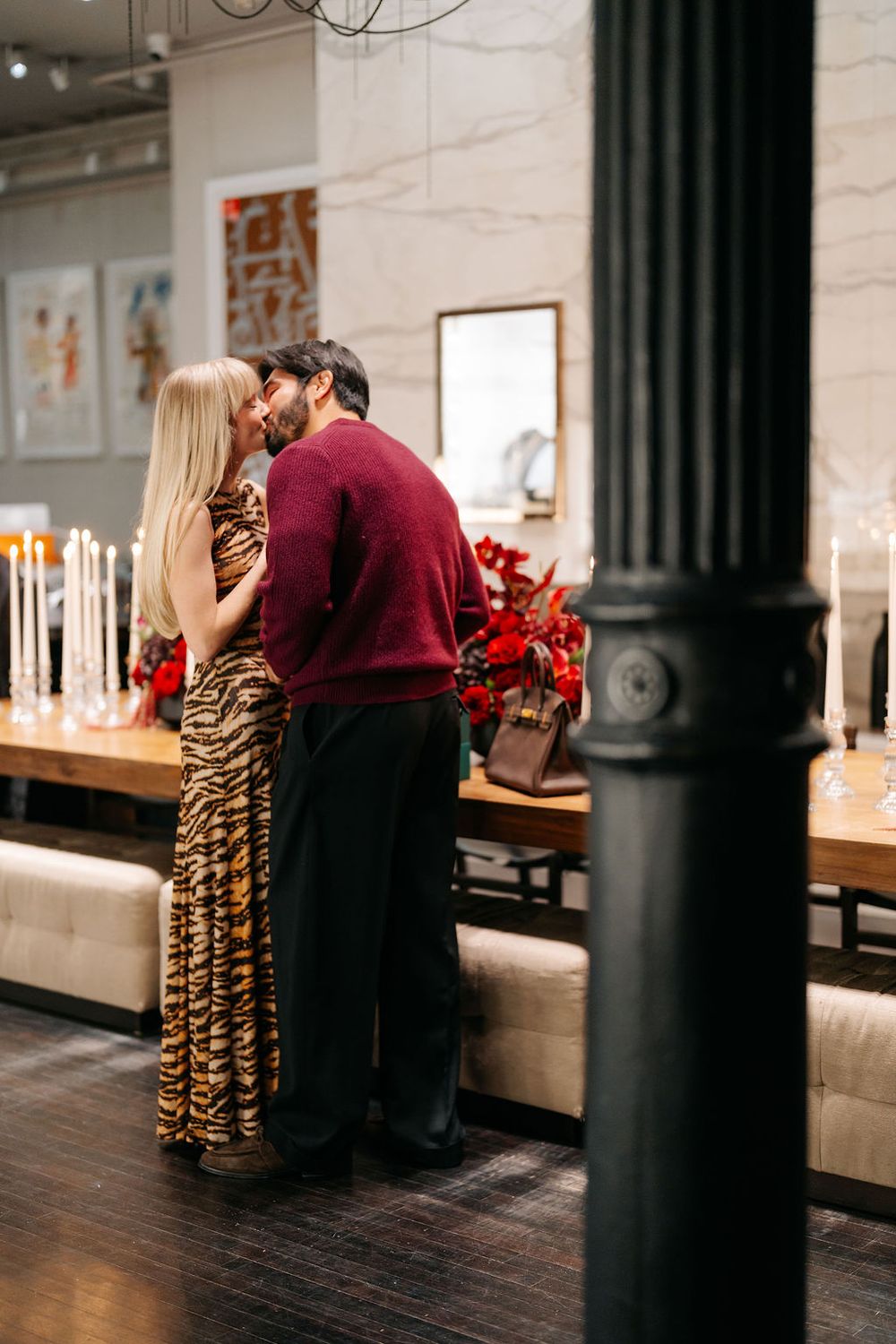 Romantic restaurant scene with candlelit wooden tables and black columns creating an intimate dining atmosphere.