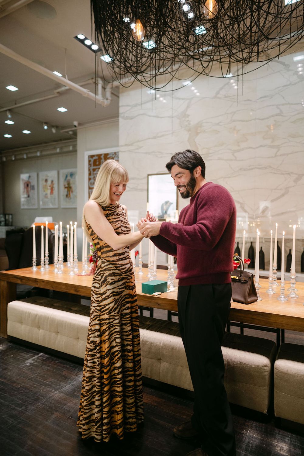 A couple shares an intimate moment in an elegant restaurant with candles and a decorative chandelier overhead.