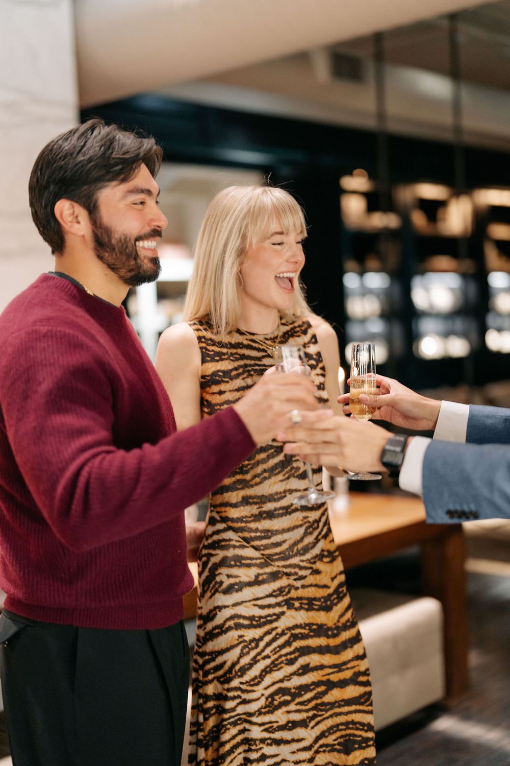 A couple in a restaurant share a joyful moment while holding drinks and laughing together.